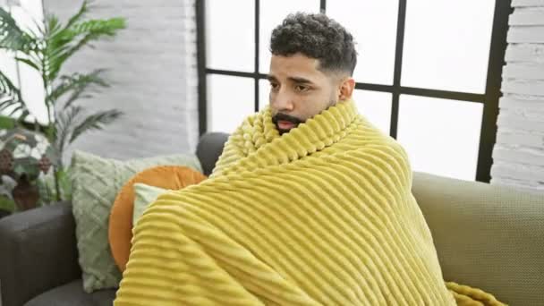 一个裹着黄色毯子的年轻人 心事重重地坐在一个舒适的房子里 里面种满了植物和垫子 — 图库视频影像