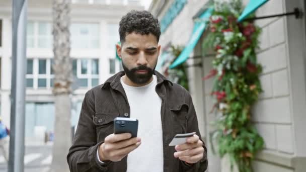 在城市街道上 一个留着胡子的英俊的恐慌男人用智能手机和信用卡 — 图库视频影像