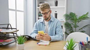 Sakallı neşeli genç bir adam modern ofis ortamında akıllı telefonunu kullanırken başarısını kutluyor..