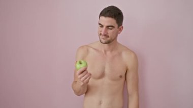 Gömleksiz, genç İspanyol bir adam, şoka girmiş, elleri ve elmalarıyla utangaç bir şekilde gözleri örtüyor, pembe izole edilmiş bir fon için korku içinde yaşarlar.