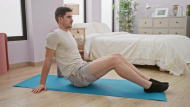 Yatak odasında egzersiz yapan yakışıklı bir adam mavi yoga minderinde egzersiz yapıyor..