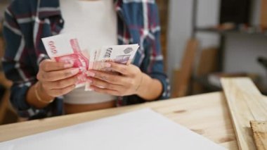 Genç Asyalı kadın marangozluk atölyesinde İzlanda kronu sayıyor.