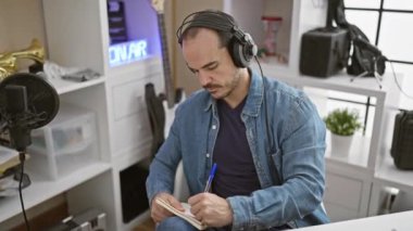 Kulaklıklı kel adam mikrofon ve enstrümanlarla bir stüdyoda müzik besteledi.