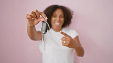 Heyecanlı siyah kadın pembe arka planda arabanın anahtarlarını tutuyor.