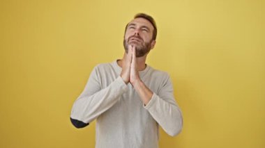 Genç İspanyol adam elleri bağlı yalvarıyor ve dua ediyor. Yüzünde umut ifadesi var. Çok duygusal ve endişeli. Yalvarıyorum. izole edilmiş sarı arkaplan