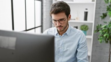 Sakallı yakışıklı İspanyol genç adam modern ofis ortamında hayal kırıklığına uğramış hissediyor, gözlüklerini çıkarıyor..