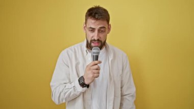 Neşeli, genç, İspanyol asıllı bir adam, canlı, izole edilmiş sarı bir duvarın karşısında, güvenli bir şekilde şarkı söylüyor. Sakallı gülüşü, müziğin keyfini çıkarırken mutluluk saçıyor..