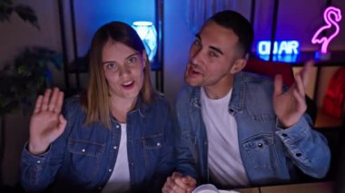 Kot pantolon giymiş gülümseyen bir kadın ve erkek, gece evde oyun oynayıp, eğlence ve teknoloji tasvir ediyorlar..