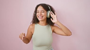 Genç, güzel İspanyol kadın müzik dinliyor ve pembe arka planda dans ediyor.