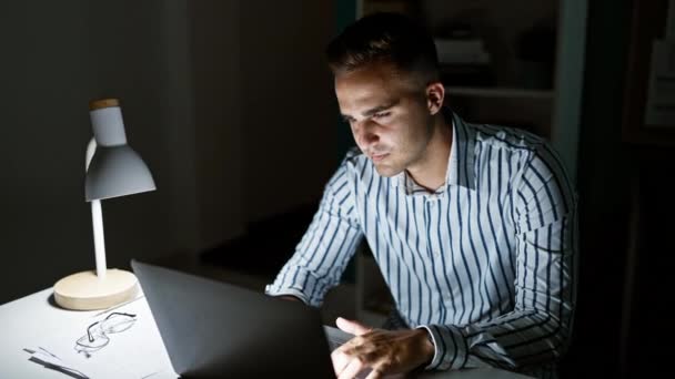 在灯光昏暗的办公室 一个专注的年轻人在笔记本电脑上工作到很晚 这增加了他的决心和专业精神 — 图库视频影像
