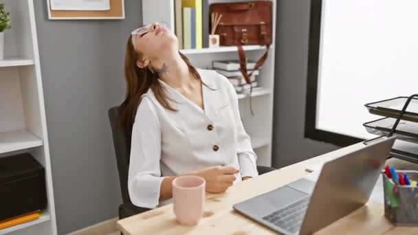 年轻的黑发女孩 看上去无聊而疲倦 一边在办公室使用笔记本电脑 一边想着双臂交叉的抑郁症状 — 图库视频影像