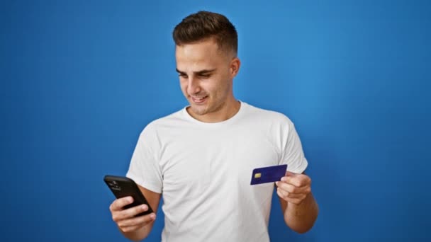 一个年轻人用智能手机拿着一张蓝色背景的信用卡 上面有网上银行或购物的图片 — 图库视频影像