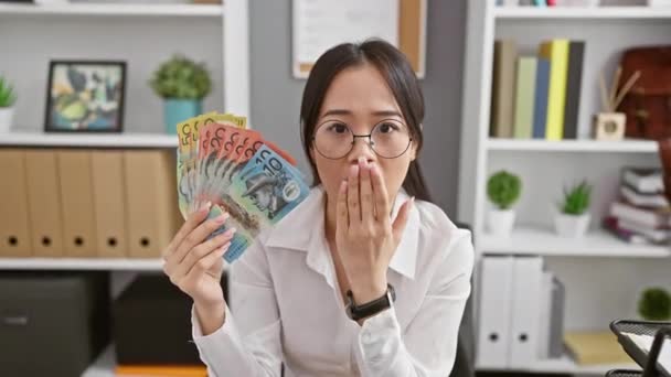 オフィスで若い中国人女性に衝撃を与え 恐怖と驚きで口を覆いました オーストラリアのドルの一握りで捕まった 言語のない表現 — ストック動画