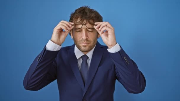 疲れた目をこするビジネスススーツで疲れた若者 孤立した青い背景に対する頭痛と視力の問題を示す表情豊かな顔 — ストック動画