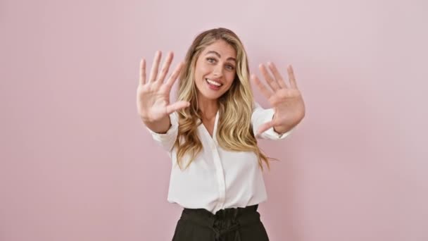 自信的年轻金发女人 穿着衬衫 站在粉色孤立的背景上 微笑着 指尖着十指 — 图库视频影像