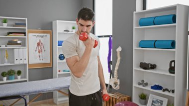 Yakışıklı İspanyol adam modern rehabilitasyon kliniğinin spor salonunda ağırlık kaldırıyor..