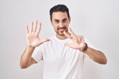 Beyaz arka planda duran yakışıklı İspanyol adam 8 numarayı gösterip işaret ederken kendinden emin ve mutlu bir şekilde gülümsüyor.. 