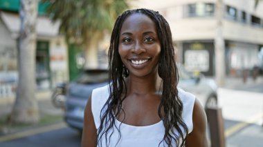 Bir şehirde açık havada duran kıvırcık saçlı, gülümseyen, Afro-Amerikan bir kadının portresi..