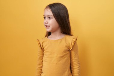 Tapılası İspanyol kız kendine güvenen bir görünüm sergiliyor, doğal gülüşüyle yan yana duruyor, yan tarafa bakıyor. İzole edilmiş sarı arka planda sakin ve rahat.