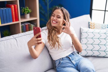 Genç İspanyol kadın akıllı telefonuyla video görüşmesi yapıyor parmaklarıyla imza atıyor, gülümseyerek mükemmel bir sembol oluşturuyor. 