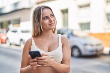 Sokakta akıllı telefon kullanan, kendine güvenen genç sarışın kadın.