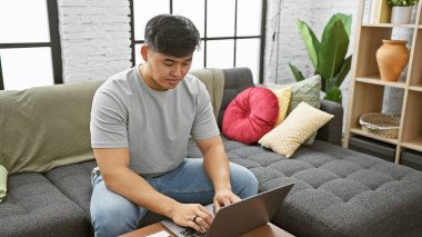 Genç Asyalı bir adam modern bir apartman dairesinde dizüstü bilgisayar kullanıyor..