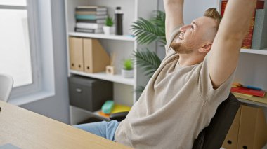 Modern ofis ortamında esneyen sakallı rahat bir genç adam pozitiflik ve iş memnuniyeti yayıyor..