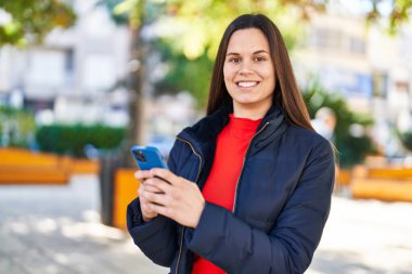 Parkta akıllı telefon kullanarak gülümseyen güzel bir İspanyol kadın.