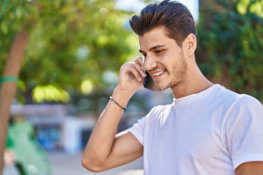 Genç İspanyol adam gülümsüyor. Parktaki akıllı telefondan konuşuyor.