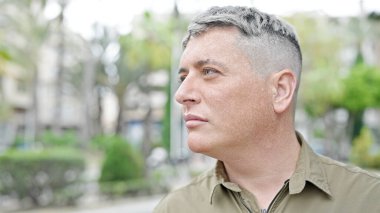 Sokakta ciddi bir ifadeyle yan tarafa bakan beyaz bir genç.