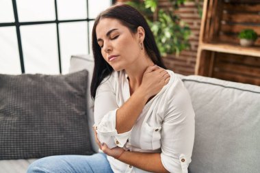 Evdeki kanepede oturan genç ve güzel İspanyol kadın boyun ağrısı çekiyor.