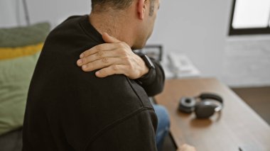 Genç bir adam evinde omuz ağrısı çekiyor, bu da sağlık hizmetlerine veya sağlık tavsiyelerine ihtiyaç olduğunu gösteriyor..