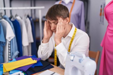 Young caucasian man tailor stressed sitting on table at tailor shop