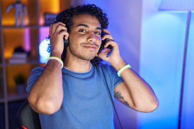 Oyun odasındaki masada kendinden emin gülümseyen genç Latin adam.