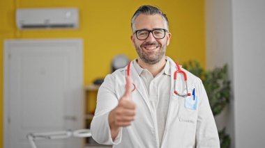 Gri saçlı doktor klinikte baş parmak yapıyor.