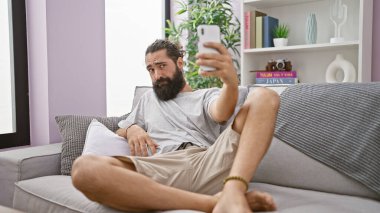 Modern apartmandaki koltukta selfie çeken sakallı İspanyol bir adam..