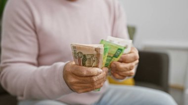 Orta yaşlı bir adam rahat bir oturma odasında Rus rublesi sayıyor..