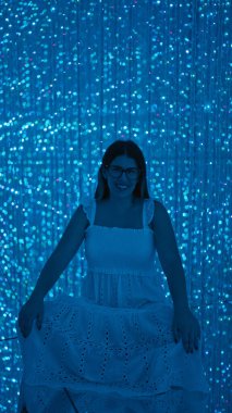 Gülümseyen güzel İspanyol kadın modern müzede fütürist sergiler sergiliyor. Lazerler, ışıklar, en iyi yenilikler.!