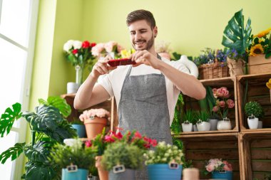 Genç beyaz erkek çiçekçi çiçekçide çiçekçide akıllı telefonla fotoğraf çekiyor.