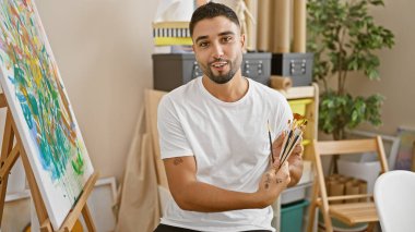 Sanat atölyesinde sakallı yakışıklı genç bir adam. Yaratıcı ekipmanlarla çevrili..