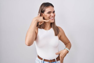 Beyaz arka planda durup gülümseyen Latin kökenli genç bir kadın telefonla el ve parmaklarıyla telefonla konuşur gibi hareket ediyor. iletişim kavramları. 