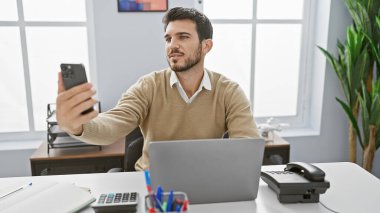 Modern ofis ortamında dizüstü bilgisayarıyla selfie çeken yakışıklı bir İspanyol..