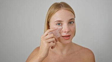 Genç sarışın kadın pembe kuvars gua kullanarak yüz masajı yapıyor.