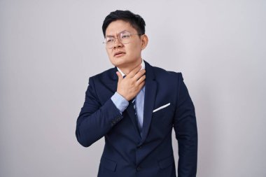 Asyalı genç bir adam iş elbisesi giyiyor ve kravat takıyor. Ağrılı boyuna dokunuyor. Grip, mantar ve enfeksiyon yüzünden boğazı ağrıyor. 