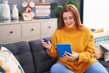 Young beautiful plus size woman using touchpad and credit card sitting on floor at home