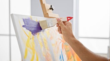 Parlak bir stüdyo ortamında, renkli bir tuvale sanatsal olarak mor boya süren bir adamın yakın çekimi..