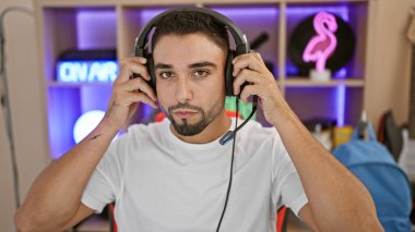 Yakışıklı sakallı adam geceleri neon ışıkları olan modern bir oyun odasında kulaklık takıyor..