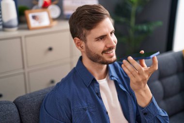 Kafkasyalı genç adam akıllı telefonda konuşuyor. Evdeki kanepede oturuyor.