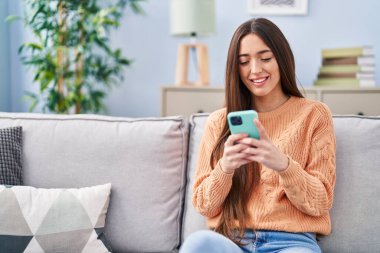 Evdeki kanepede oturan akıllı telefon kullanan genç, güzel İspanyol kadın.