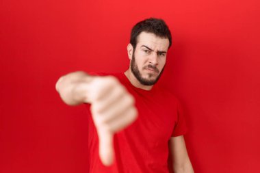 Genç, İspanyol asıllı, sıradan kırmızı tişört giyen mutsuz, kızgın, reddedilmiş ve olumsuz jestler yapan bir adam. kötü ifade. 